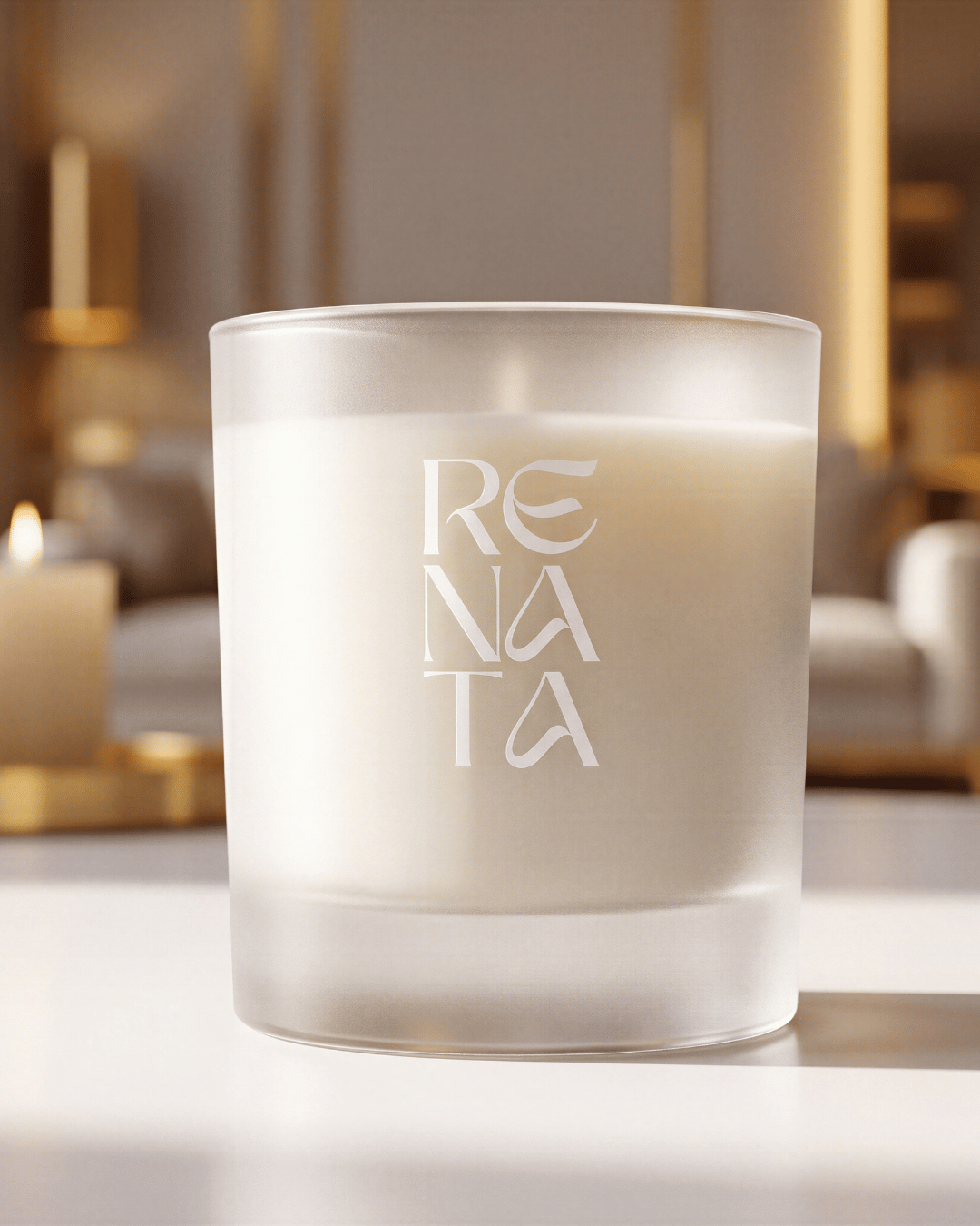 A frosted glass candle jar with the brand name 'RENATA' printed vertically in white on the front, filled with white wax and set against a softly blurred warm interior background.